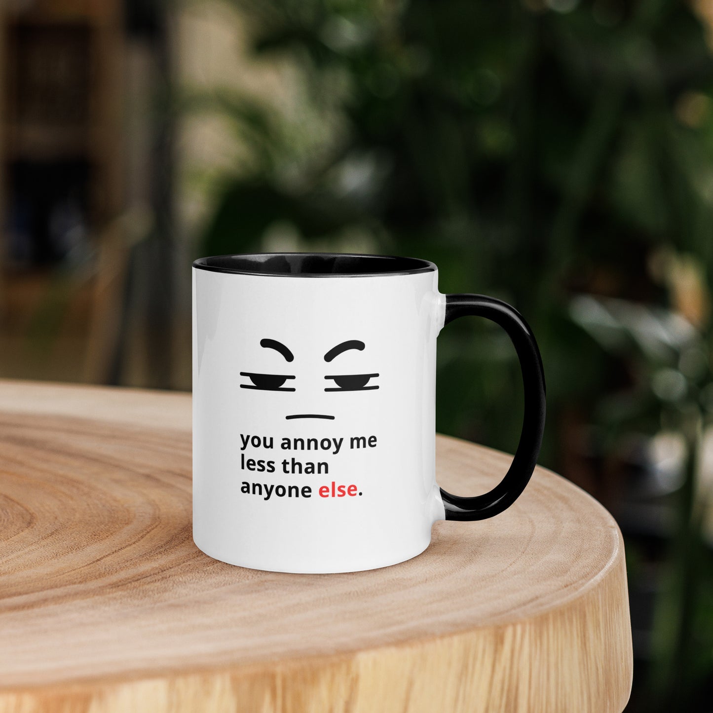 Snarky relationship mug with “You Annoy Me Less Than Anyone Else” text and frowning face design black inside and handle on table 